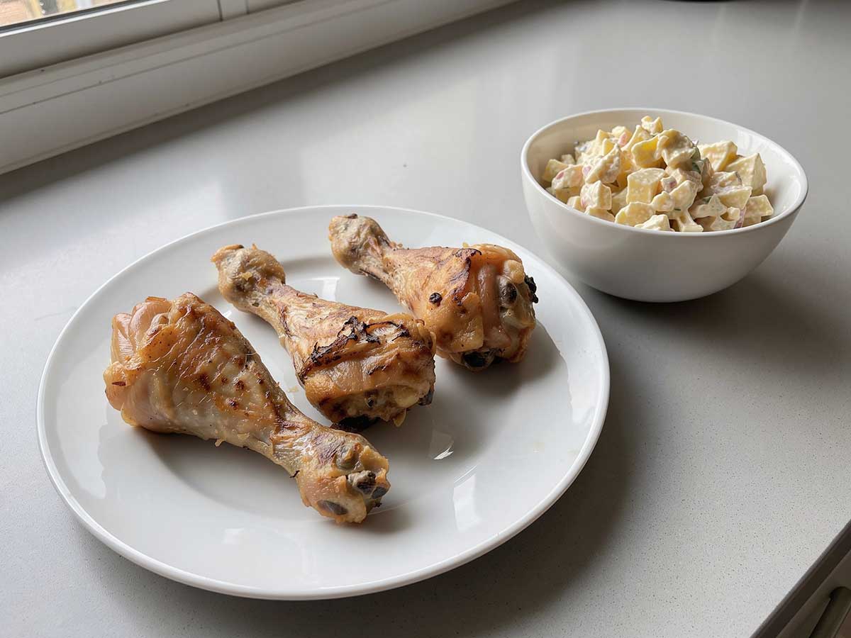 Een bord met 3 geroosterde drumsticks met aardappelsalade.