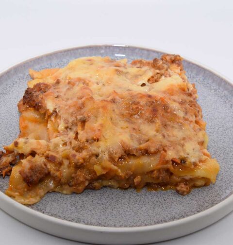 Een portie lasagne met tomatensaus op een bordje.