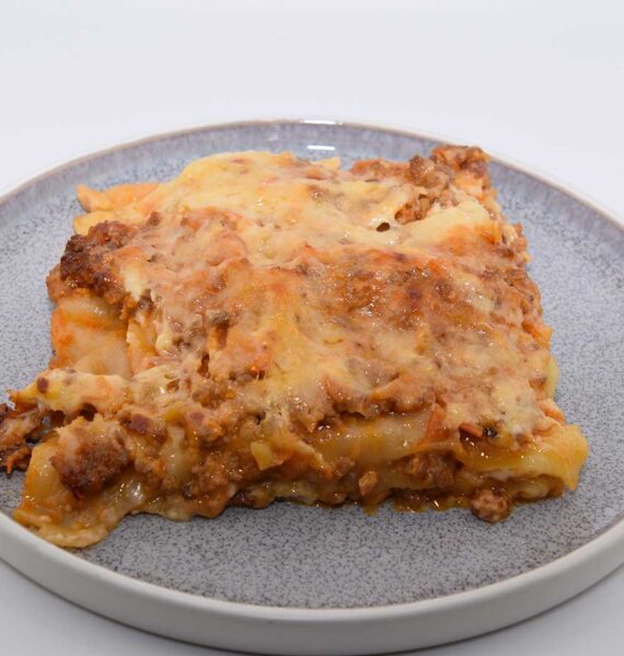 Een portie lasagne met tomatensaus op een bordje.