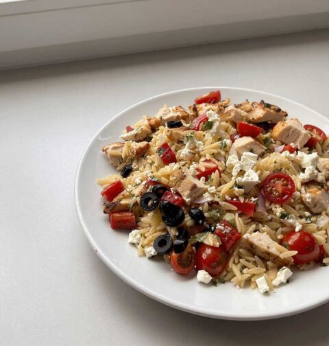 Een bord met daarop een portie orzosalade met kip.