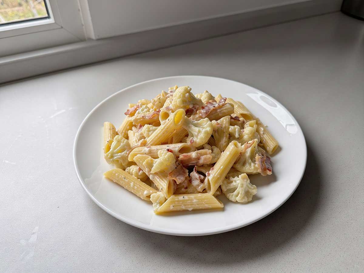 Een bord met daarop een portie pasta met bloemkool.