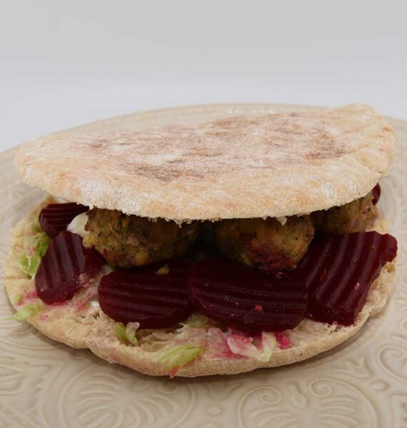 Een bord met een pitabroodje gevuld met falafel, knoflooksaus en zoetzure bieten