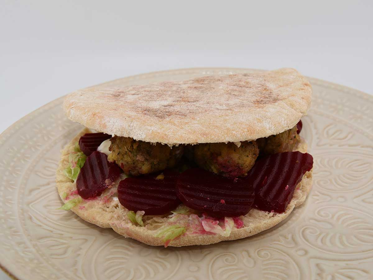 Een bord met een pitabroodje gevuld met falafel, knoflooksaus en zoetzure bieten