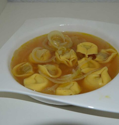 Een soepbord met uiensoep met tortellini.
