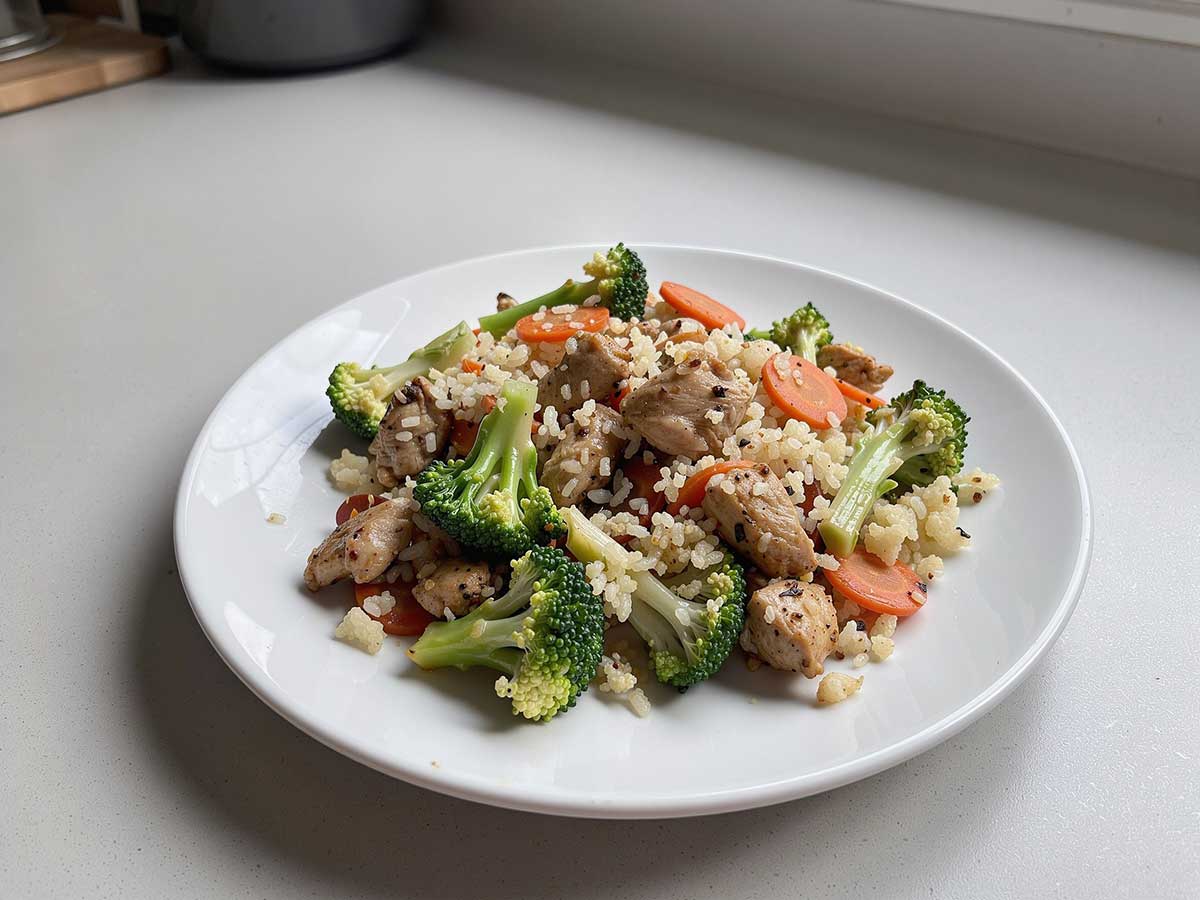 Een bord met daarop wokschotel met kip, broccoli, wortel, bloemkoolrijst.
