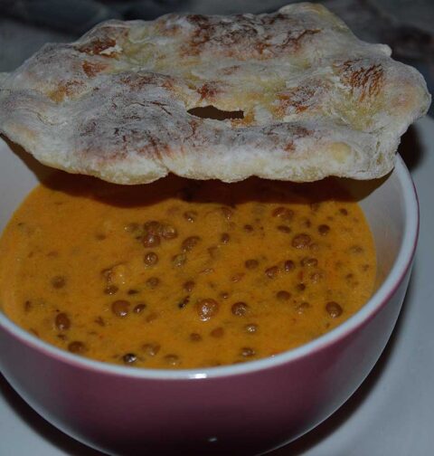 Een soepkom met wortel linzensoep en een stuk naanbrood er bovenop.