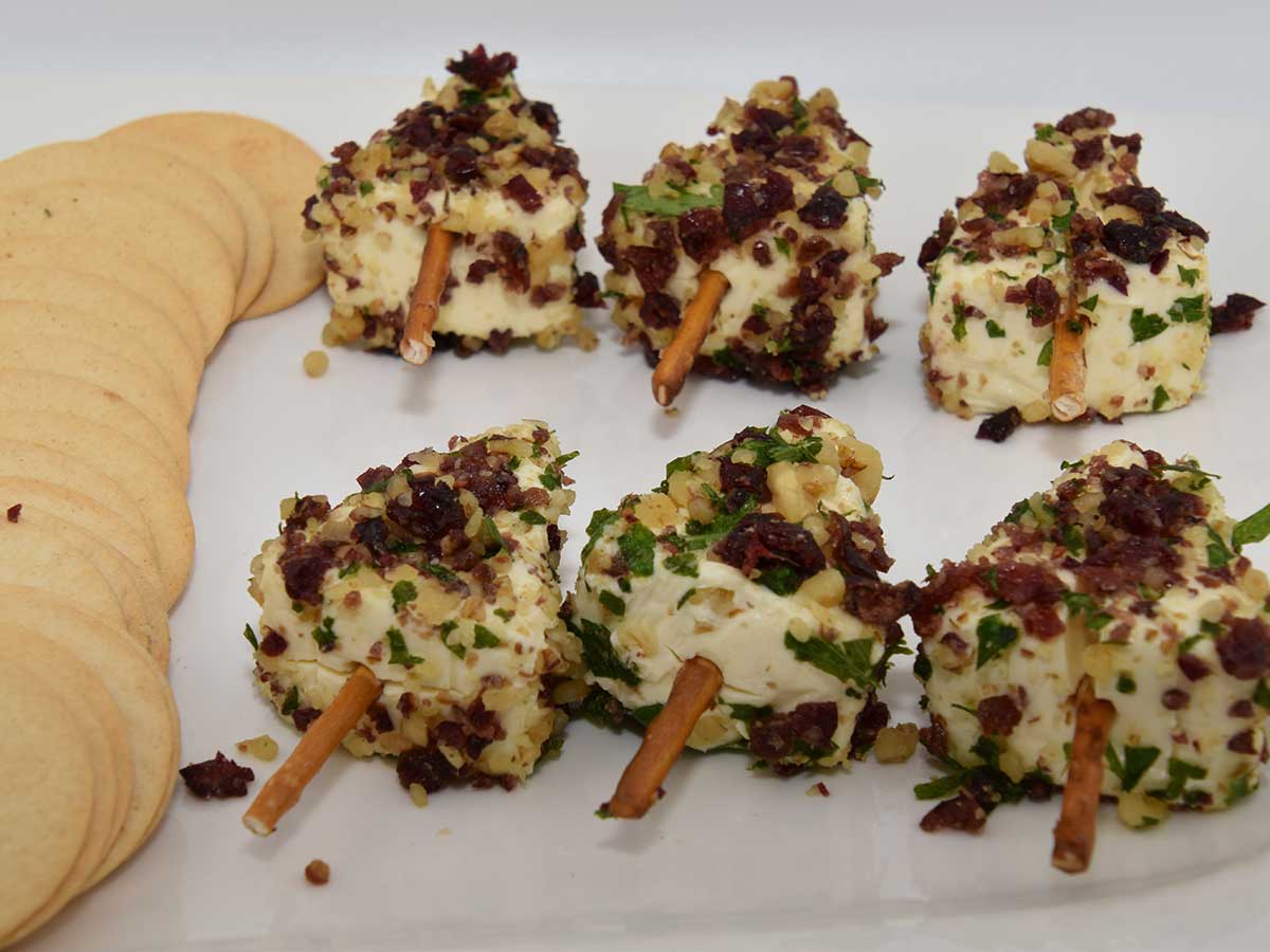 6 kaas-walnoot-cranberries op een stokje op een wit bordje, met crackers.